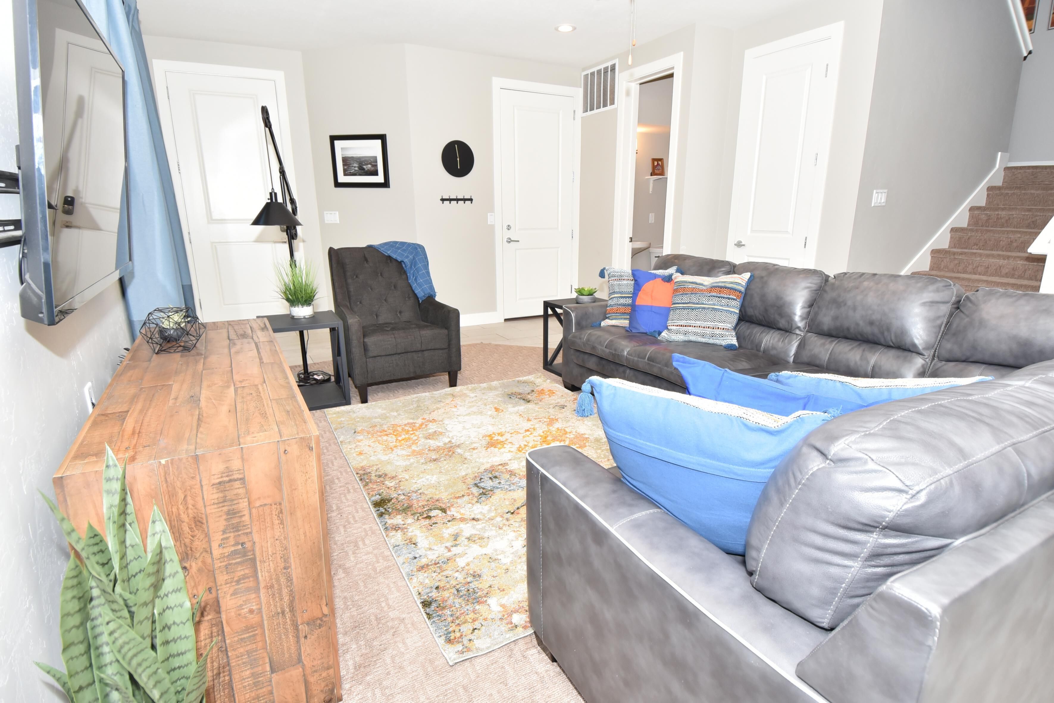 A living room with a wooden coffee table, a grey sofa with blue cushions, a black armchair, and a patterned rug.