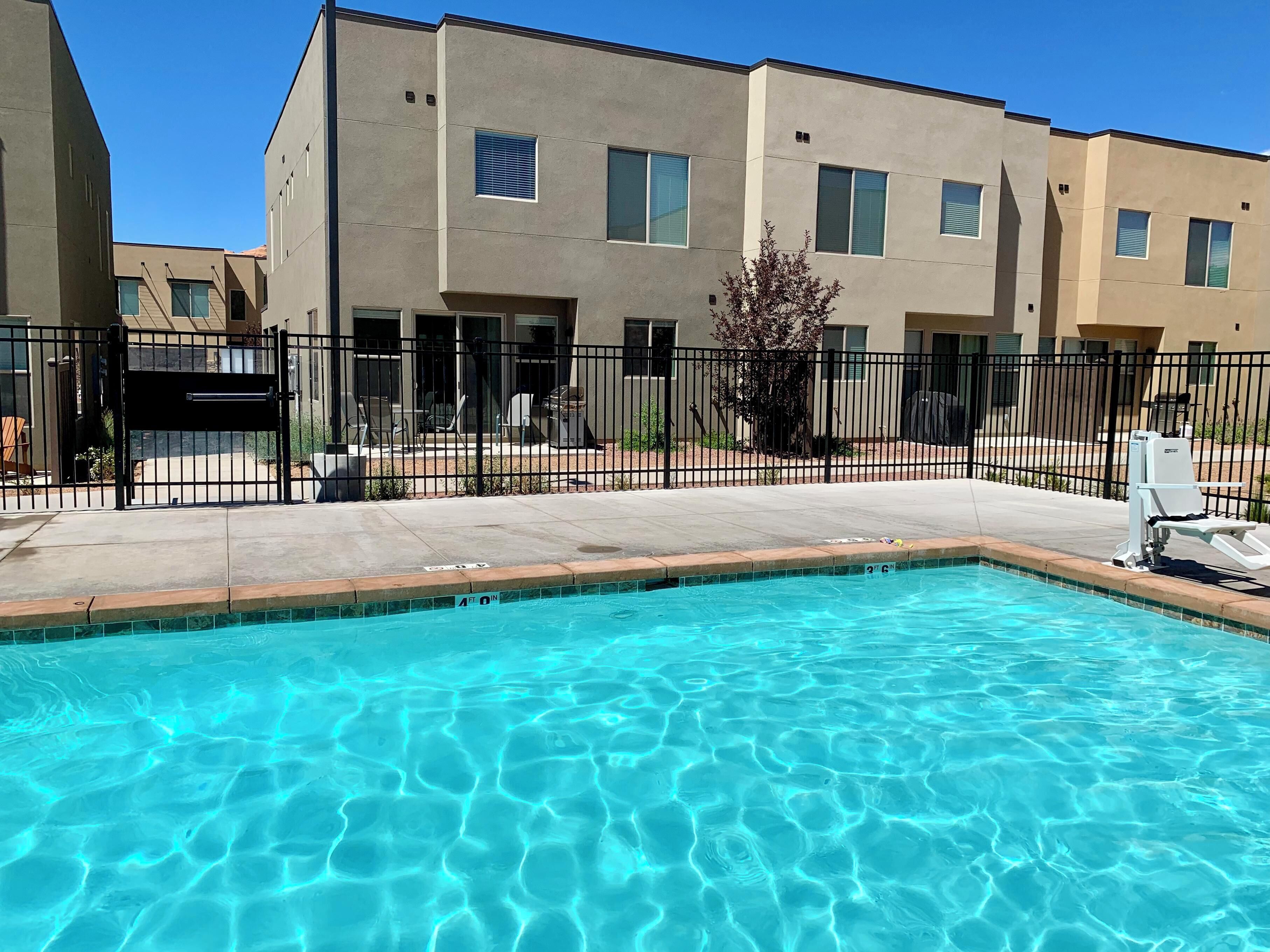 A swimming pool with clear blue water, surrounded by a concrete deck and a black metal fence.