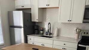 A modern kitchen with white cabinetry, a wooden island with two stools, a stainless steel refrigerator, a coffee maker, and a microwave. - Tidy Apartment Near Hospital/PCC (Pensacola)