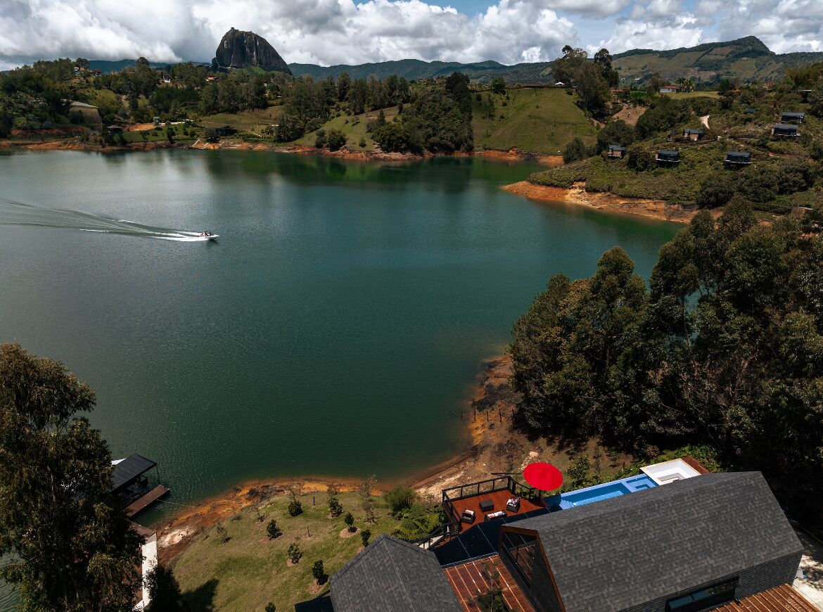 Una propiedad frente al lago con vista a un barco en el agua, un paraguas rojo y una terraza con mobiliario exterior.