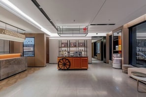 A modern hotel lobby with a reception desk, seating area, and a central island with a decorative wheel. - Homeinn Plus Hotel (Shanghai Bund Nanjing Road Pedestrian Street) (Shanghai)