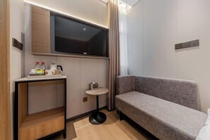 A modern hotel room with a flat-screen TV mounted on the wall, a small round table with a coffee maker, and a grey sofa. - Homeinn Plus Hotel (Shanghai Bund Nanjing Road Pedestrian Street) (Shanghai)