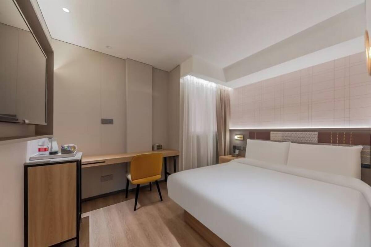 A hotel room with a large bed, a desk, a chair, and a small cabinet.