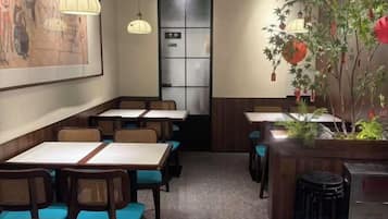 A restaurant interior with tables and chairs, a refrigerator, and decorative plants.