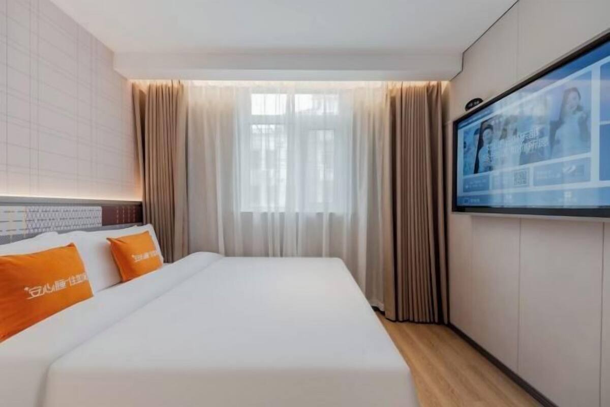 A hotel room with a bed, curtains, a television, and a window.