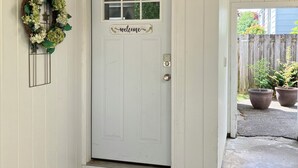 A white door with a 'welcome' sign, a wreath, and a doormat. - Charming cottage in scenic Seattle with AC, WiFi, and all the comforts of home. (Seattle)