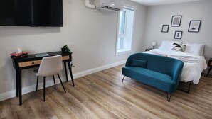 A modern bedroom with a bed, a desk, a chair, a TV, and a window.