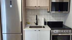 A compact kitchen with a stainless steel refrigerator, a microwave, a sink, and a stove.