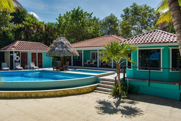 A pool area with a tiled pool, lounge chairs, and a thatched roof structure. - 6-Guest Beachfront Oasis w/ Private Pool (Placencia)