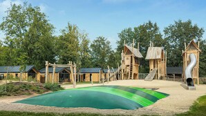 Ein Spielplatz mit Holzspielgeräten und einer grünen, gummiartigen Oberfläche.
