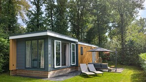 Ein modernes, eingeschossiges Haus mit großen Glasfenstern, einer Holzterrasse und Sitzgelegenheiten im Freien.