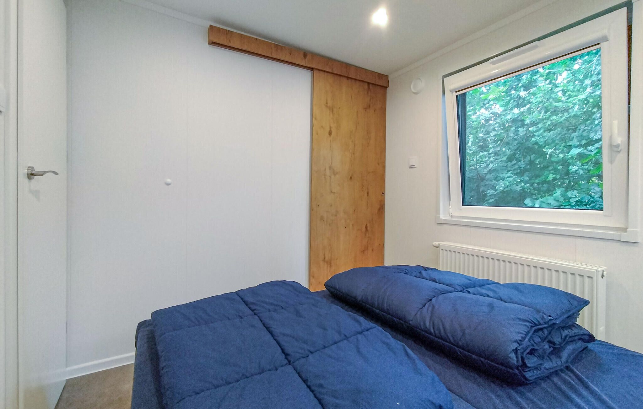 A bedroom with a bed, a window with a view of trees, a radiator, and a wooden beam above the door.