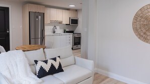 A modern kitchen with a refrigerator, microwave, stove, and cabinets. There is a white sofa with a black and white pillow in the living area. - 1 Bedroom Unit with living space and full kitchen Prime Downtown location (Kitchener)