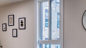 A modern living room with a sofa, a round wooden table, and two chairs. There is a large window with a view of buildings outside. - 1 Bedroom Unit with living space and full kitchen Prime Downtown location (Kitchener)