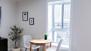 Une pièce moderne avec une table à manger en bois, deux chaises blanches, une plante en pot et des œuvres d’art encadrées accrochées au mur.