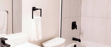 Een moderne badkamer met een wit wastafelmeubel, een toilet, een bad en een douche.