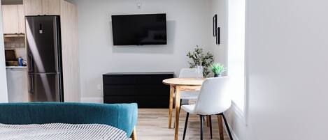 A modern bedroom with a bed, a dining area with a table and chairs, a black cabinet, and a TV mounted on the wall.