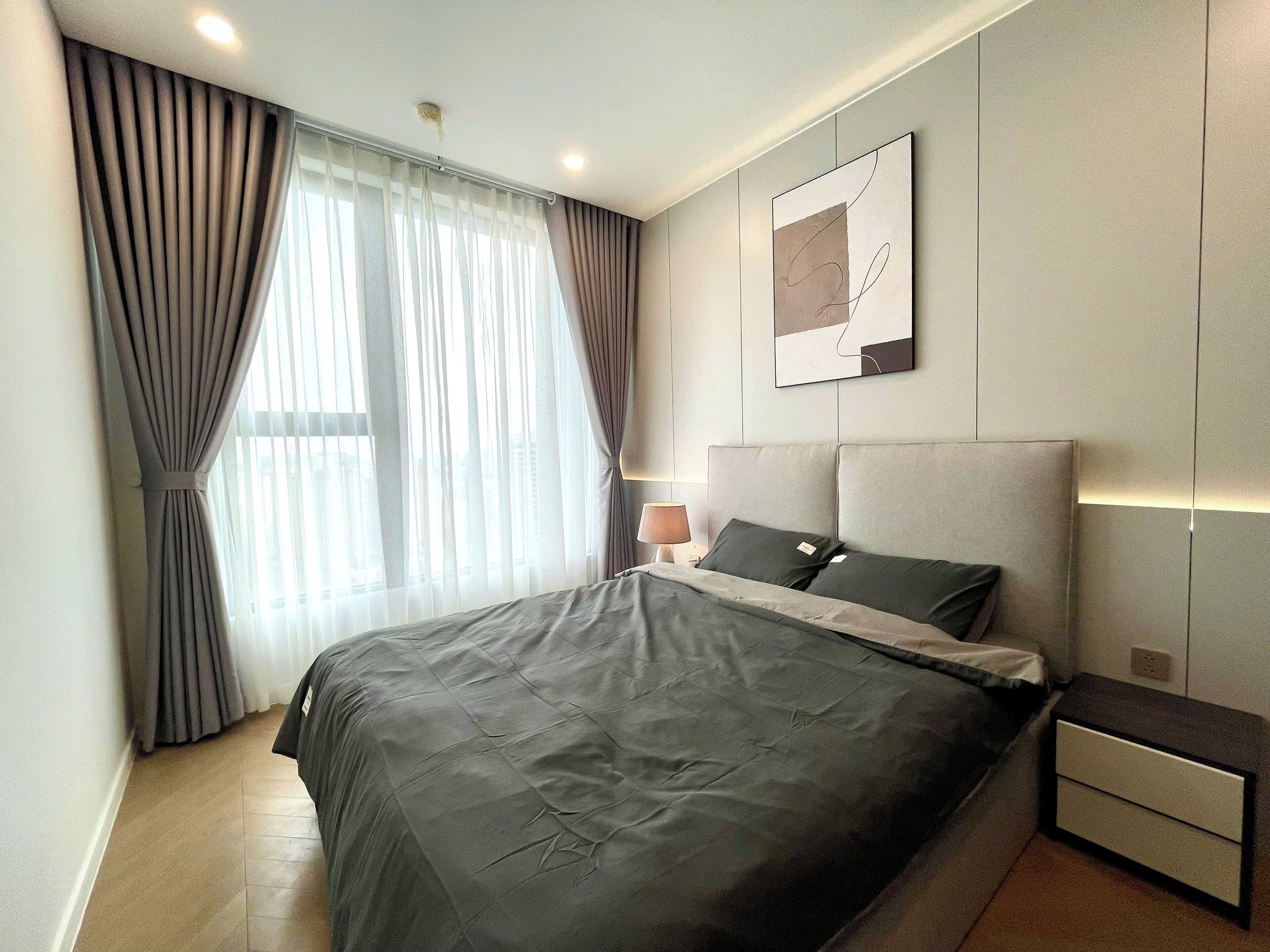 A modern bedroom with a large bed, a bedside table, a lamp, and a wall-mounted artwork.