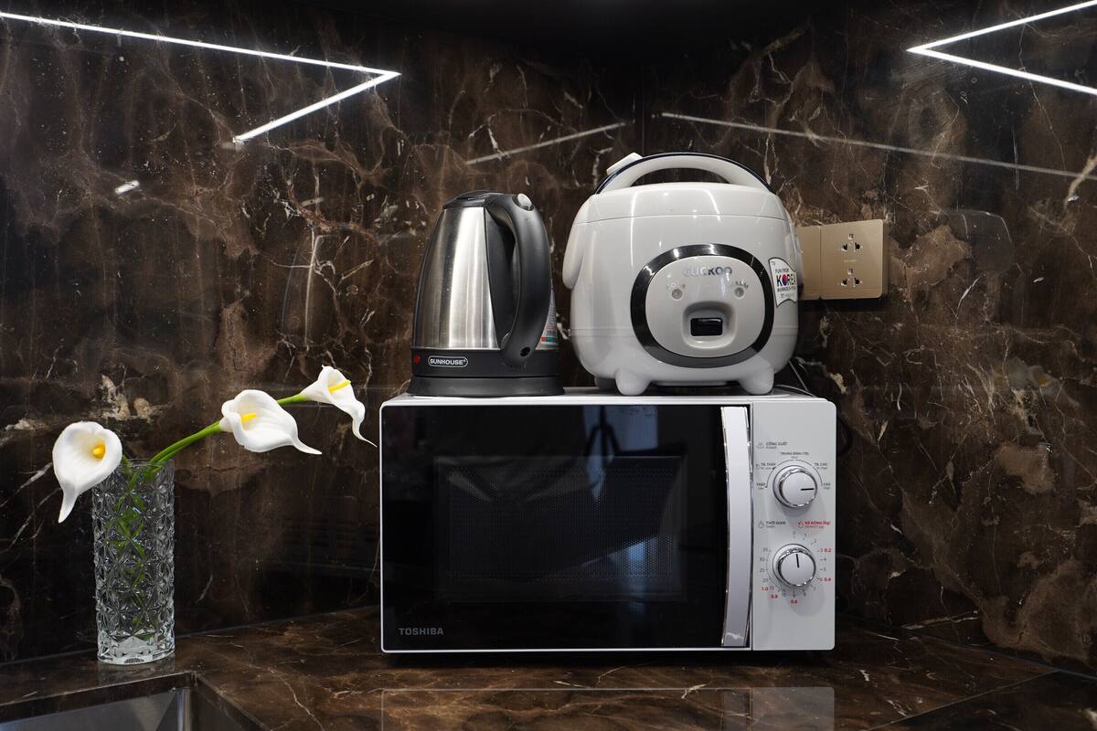 Een keuken met een magnetron, een waterkoker en een vaas met bloemen op een marmeren aanrecht.