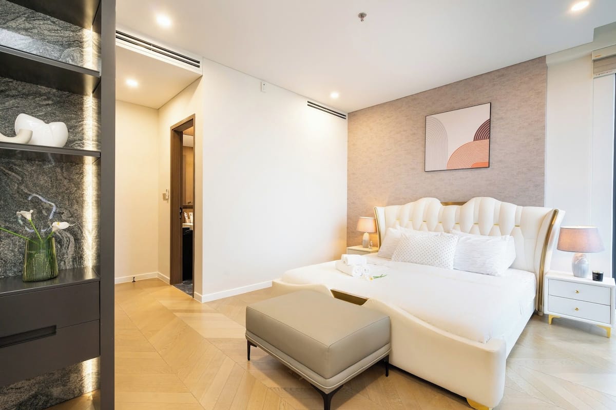 Een moderne slaapkamer met een groot bed, een nachtkastje en een marmeren plank met decoratieve objecten.