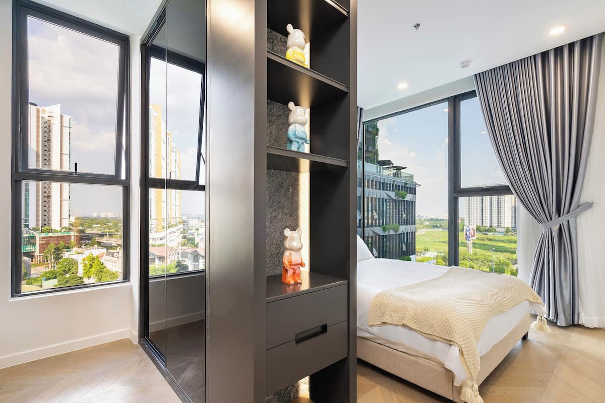 Een moderne slaapkamer met een groot raam, een bed, een nachtkastje en een plank met decoratieve objecten.