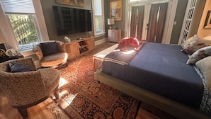 Een slaapkamer met een groot bed, een televisie, een stoel en een vloerkleed.