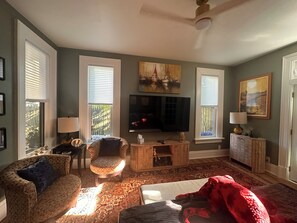 Un salon avec une télévision, deux fauteuils, un canapé, une couverture rouge et un tapis à motifs.