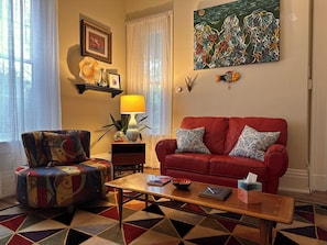 A living room with a red sofa, patterned armchair, a coffee table, and a painting on the wall.