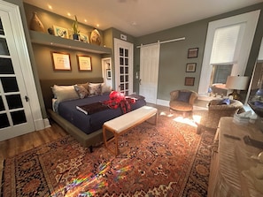 A bedroom with a bed, bench, chair, and a patterned rug.