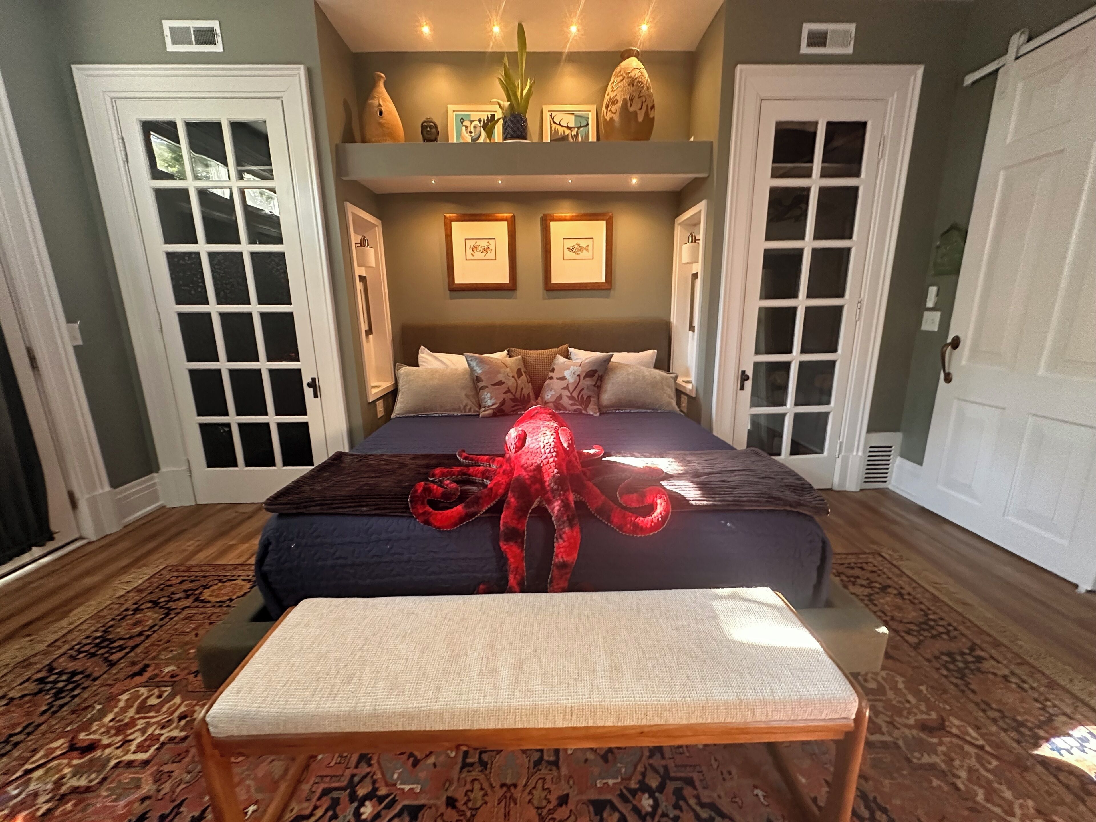 A bedroom with a large bed, a bench, a decorative octopus, and a patterned rug.