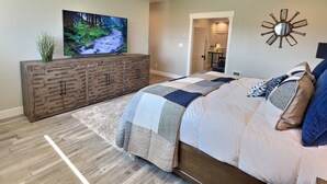A bedroom with a large bed, a TV on a wooden cabinet, a decorative wall piece, and a hallway leading to a bathroom. - RAINEY CREEK RETREAT (Swan Valley)