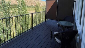 A balcony with a view of a hilly landscape, a table and chairs, and a black metal railing. - RAINEY CREEK RETREAT (Swan Valley)