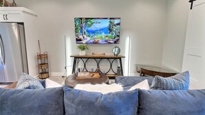 A living room with a grey sofa, a TV on a stand, a bookshelf, and a small table with a plant. - RAINEY CREEK RETREAT (Swan Valley)