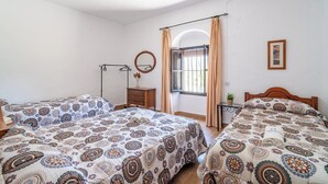 Ein Schlafzimmer mit zwei Betten, einem Holzkopfstück, einem kleinen Tisch, einem Spiegel und einem Fenster mit Vorhängen.