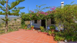A house with a tiled patio, surrounded by lush greenery and flowering plants. - Casa Fuentezuelas Sayalonga by Ruralidays (Málaga)