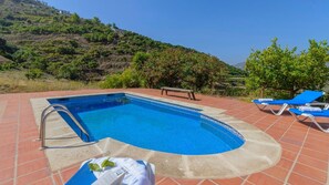 Una piscina de borde curvo, rodeada de sillas reclinables azules y una escalera metálica.