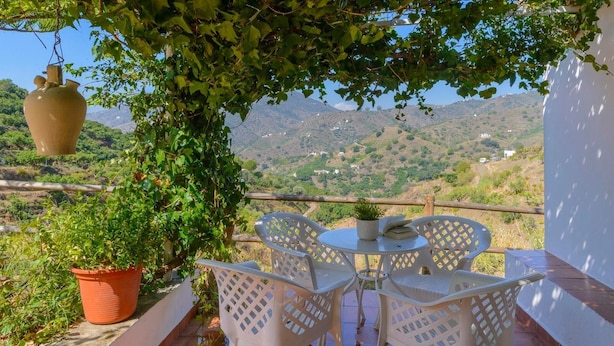 A terrace with white lattice chairs and a table, surrounded by greenery and overlooking a mountainous landscape. - Casa Fuentezuelas Sayalonga by Ruralidays (Málaga)