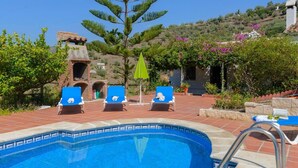 A swimming pool with blue tiles, three blue lounge chairs, a green umbrella, and a brick structure in the background. - Casa Fuentezuelas Sayalonga by Ruralidays (Málaga)