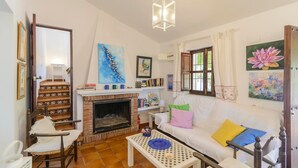 A living room with a fireplace, white furniture, and various artworks on the walls. - Casa Fuentezuelas Sayalonga by Ruralidays (Málaga)