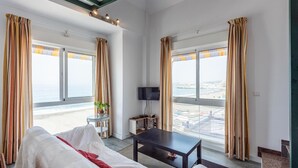 Une chambre d’hôtel avec un lit, une petite table, une télévision et de grandes fenêtres équipées de rideaux.