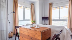 Une chambre d’hôtel avec un lit, un bureau en bois sur lequel se trouvent deux tasses, une chaise, un téléviseur et une fenêtre avec des rideaux.
