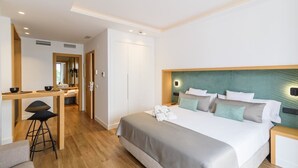 Une chambre d’hôtel moderne, dotée d’un grand lit, d’un bureau avec des tabourets et d’une salle de bain visible à travers une porte ouverte.
