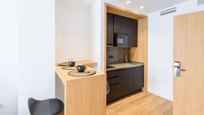 Une cuisine compacte équipée d’un micro-ondes, d’un évier et de meubles de rangement sombres. On y trouve une petite table à manger avec deux tasses et un set de table.