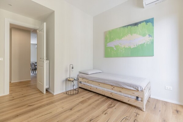Un dormitorio con una cama de madera, una mesita de noche pequeña y un cuadro abstracto verde en la pared.