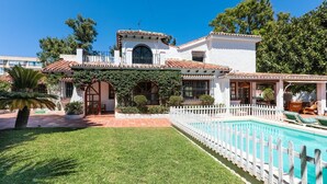 A two-story house with a swimming pool, surrounded by a white picket fence, and a well-maintained lawn.