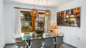 A dining area with a glass table, grey chairs, a wicker centerpiece, and a wall-mounted lamp.