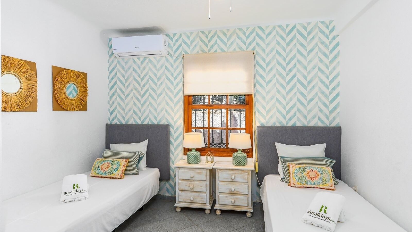 Een kamer met twee eenpersoonsbedden, een bureau met lamp, een raam met uitzicht en een behang met patroon.
