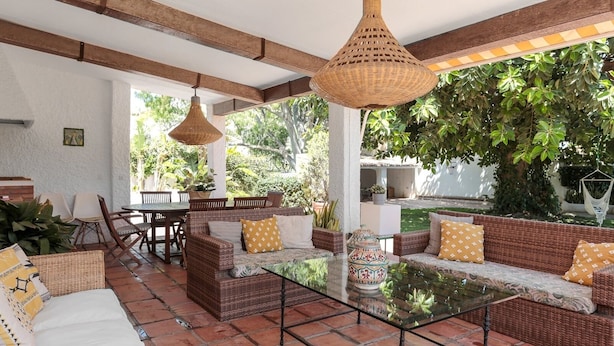 An outdoor patio area with wicker furniture, a glass-top table, and hanging wicker lamps.