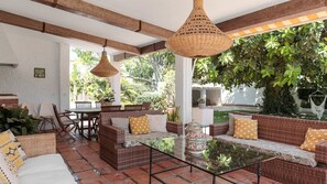 Un patio al aire libre con mobiliario de mimbre, una mesa con cubierta de vidrio y lámparas colgantes de mimbre.