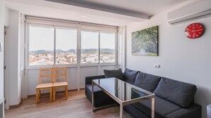 Ett modernt vardagsrum med ett stort fönster, en soffa, en trästol och ett soffbord i glas.
